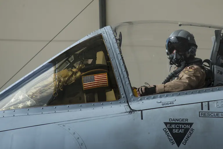 An Air Force pilot in helmet and oxygen mask seated in the cockpit of an A-10 Thunderbolt II