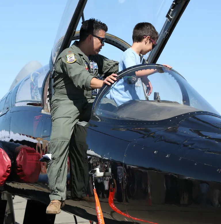 An airman showing a boy the cockpit of a T-38 Talon on the flightline